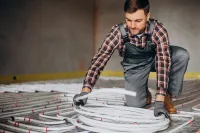 Instalator układa rury ogrzewania podłogowego na izolacji w budowanym domu